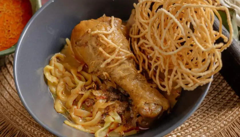 Khao Soi: ein Hühnerbein auf Nudeln in cremiger Kokosmilch-Currysauce, garniert mit knusprigen Nudeln.
