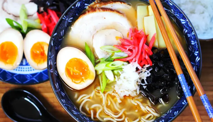 Eine Schüssel Ramen mit perfekt gekochten ramen eiern, Schweinefleisch, Bambussprossen und Frühlingszwiebeln. Daneben liegen weitere halbe Eier.