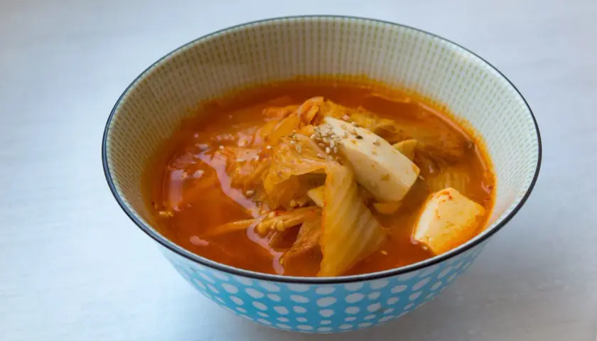 Eine Schüssel mit dampfender Kimchi-Suppe, garniert mit Tofuwürfeln und Sesam.