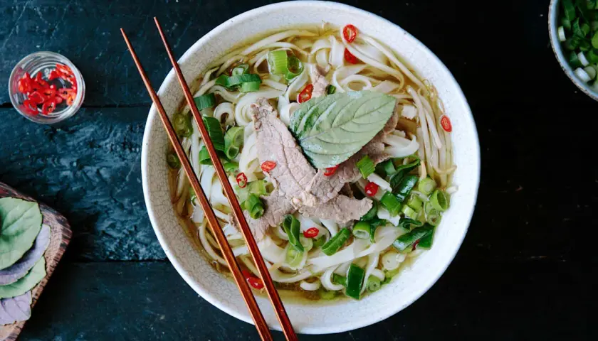 Eine Schüssel dampfendes Pho mit dünnen Rindfleischscheiben, Reisnudeln, Frühlingszwiebeln und Chili. Ein perfektes Pho-Rezept für kalte Tage.