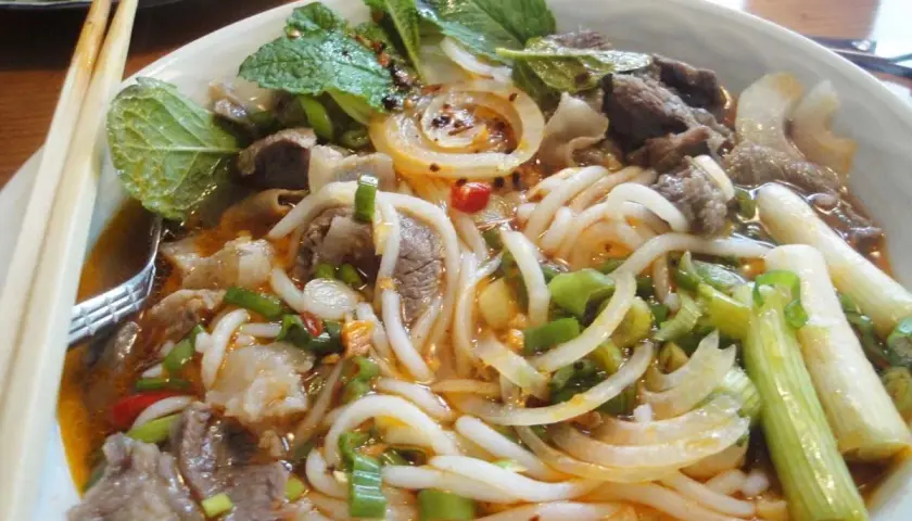Eine Schüssel Bun Bo Hue mit Rindfleisch, Nudeln, Zwiebeln, Frühlingszwiebeln und Minze.