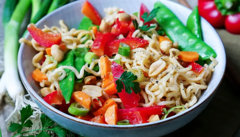Bunter mie nudelsalat mit Erdnüssen, Paprika, Zuckerschoten und Karotten, garniert mit Petersilie.