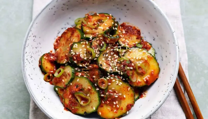 Ein Schüssel mit einem würzigen Gurken-Kimchi-Salat, garniert mit Sesam und Frühlingszwiebeln.