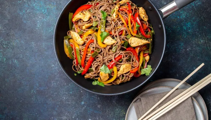 Wok-Gericht mit chinesischen Eiernudeln, Hähnchenstreifen und bunten Paprikastreifen, garniert mit Koriander.