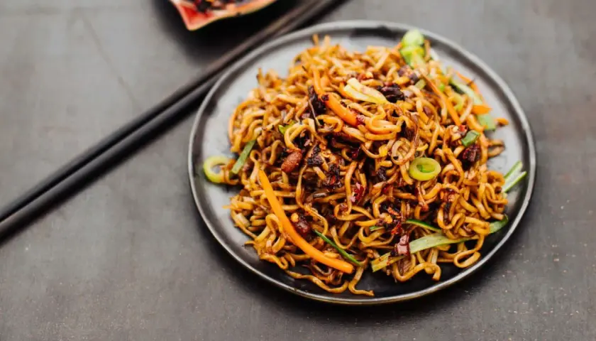 Ein Teller mit leckerem Chow Mein, garniert mit Frühlingszwiebeln und Karotten. Perfekt für ein schnelles, herzhaftes Essen.