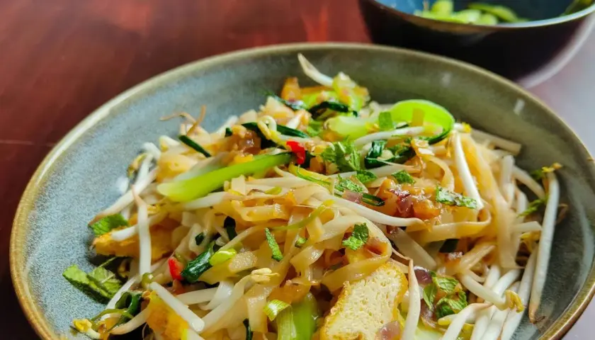Ein Teller mit dampfendem Pho Xao, garniert mit frischen Kräutern und knackigen Sojasprossen.