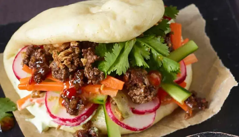 Ein saftiger Bao Burger mit Hackfleisch, knackigem Gemüse wie Karotten, Radieschen und Gurken, garniert mit Koriander.