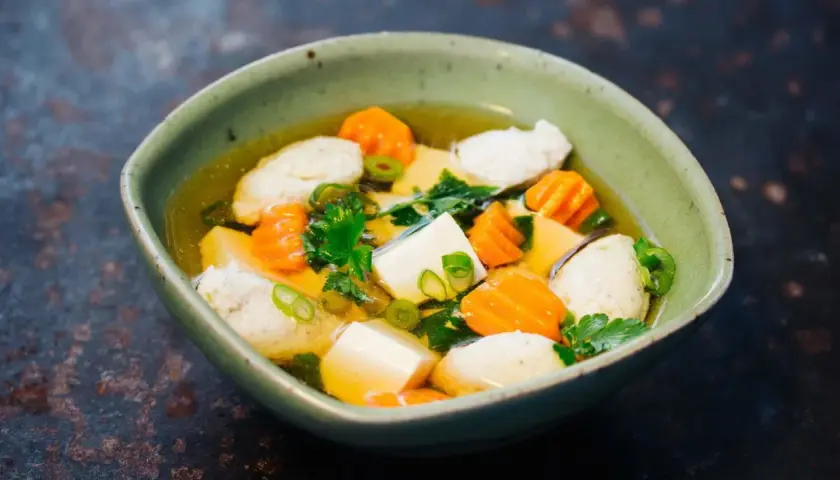 Eine Schüssel Hu Tieu Suppe mit Tofu, Karotten und Fleischbällchen, garniert mit Frühlingszwiebeln und Petersilie.