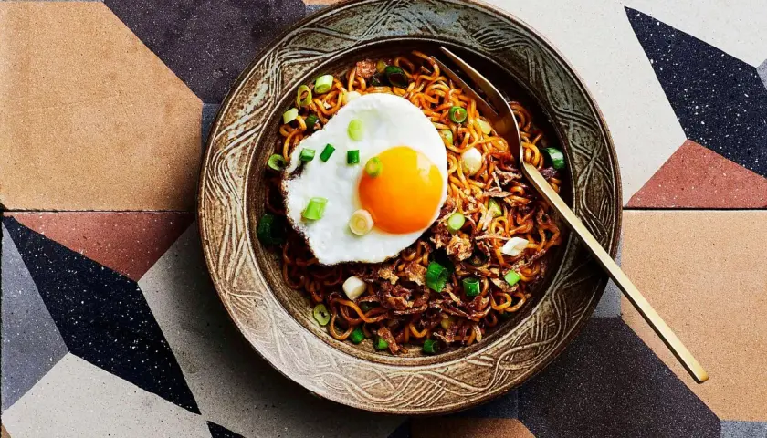 Schüssel mit Mie Goreng, garniert mit einem Spiegelei und Frühlingszwiebeln, auf einem geometrischen Fliesenmuster.