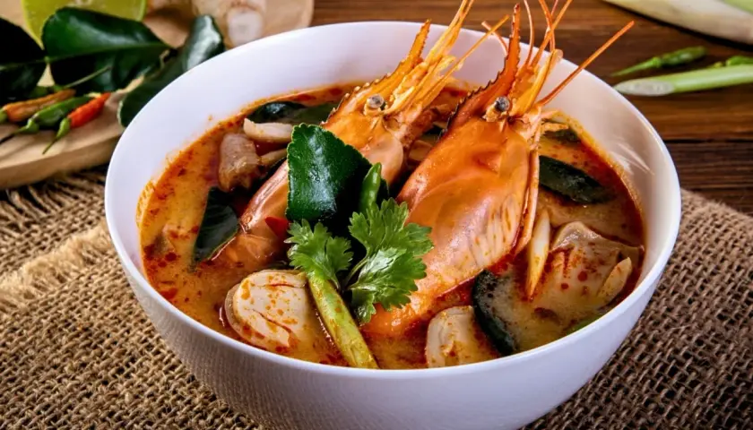 Eine Schüssel Tom Yum Suppe mit Garnelen, Pilzen und Kaffirlimettenblättern, garniert mit Koriander.