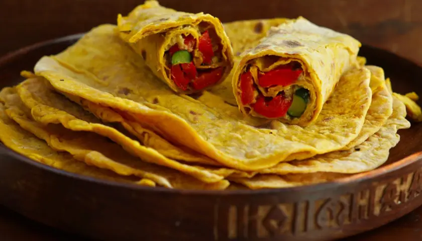 Chapati-Rezept: Fladenbrot gefüllt mit roten Paprika und Gurke, auf einem Stapel weiterer Chapati in einer Holzschale.