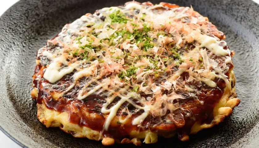 Ein herzhaftes Okonomiyaki Hiroshima, übergossen mit Sauce und Mayonnaise, bestreut mit Bonitoflocken und Schnittlauch.