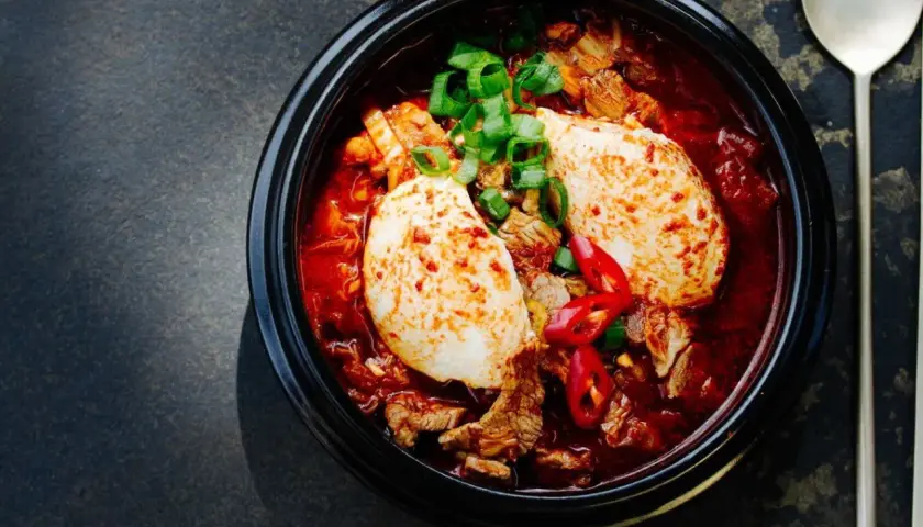 Herzhaftes Kimchi Jjigae mit Tofu, Rindfleisch und Frühlingszwiebeln, garniert mit Chilischeiben.