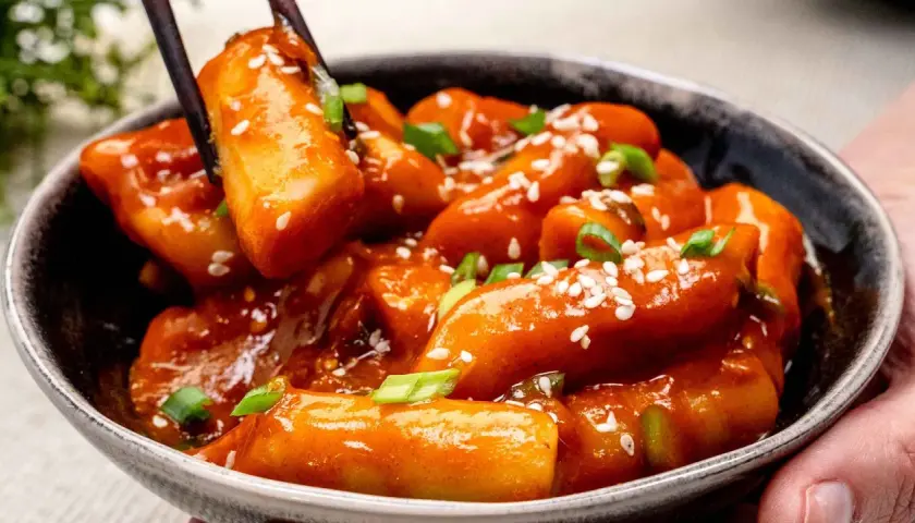 Schüssel mit würzigem Tteokbokki, Reiskuchen in scharfer Sauce, garniert mit Sesam und Frühlingszwiebeln.