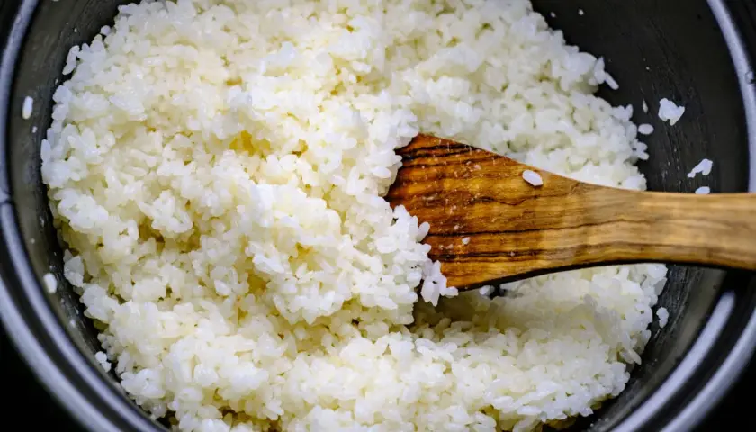 Frisch gekochter Reis wird mit einem Holzlöffel vermischt, bereit für Sushi-Essig.