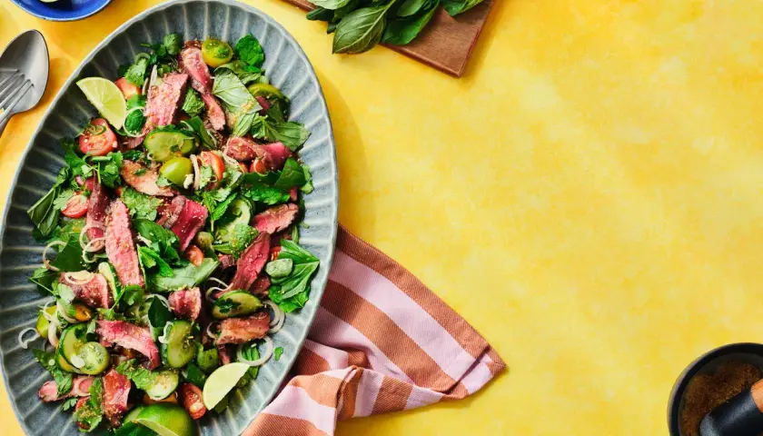 Würzig-frischer Rindfleischsalat Thai mit zarten Rindfleischstreifen, Gurken, Tomaten und Kräutern, garniert mit Limettenspalten.