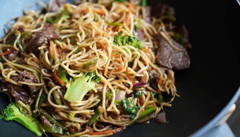 Leckere asiatische Nudeln kochen mit Rindfleisch, Brokkoli, Karotten und Paprika in einem Wok.