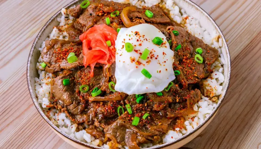 Eine köstliche japanische Bowl mit Reis, zartem Rindfleisch, einem pochierten Ei, eingelegtem Ingwer und Frühlingszwiebeln.