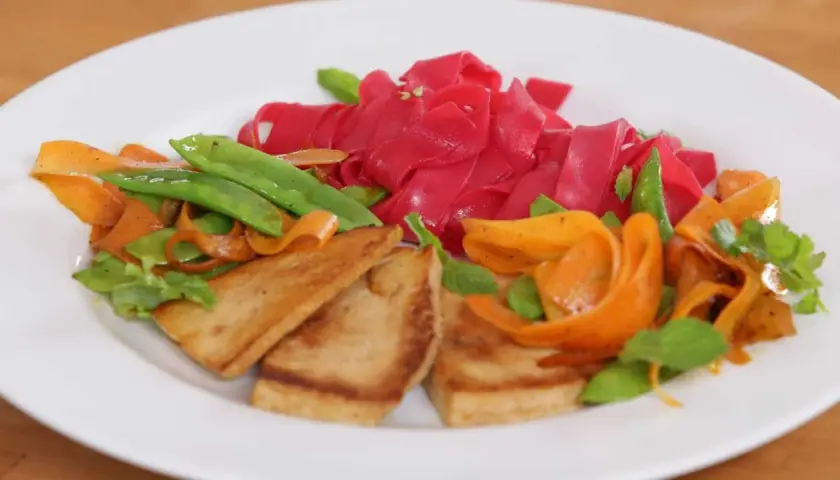 Bunte Reisnudeln kochen mit gebratenem Tofu, Karotten und Zuckerschoten. Ein farbenfrohes Gericht, das Lust auf mehr macht.