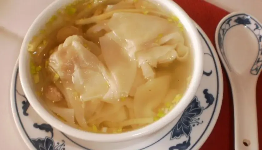 Eine Schüssel mit dampfender Wan-Tan-Suppe, gefüllt mit zarten Teigtaschen und Garnelen, bereit zum Genießen.