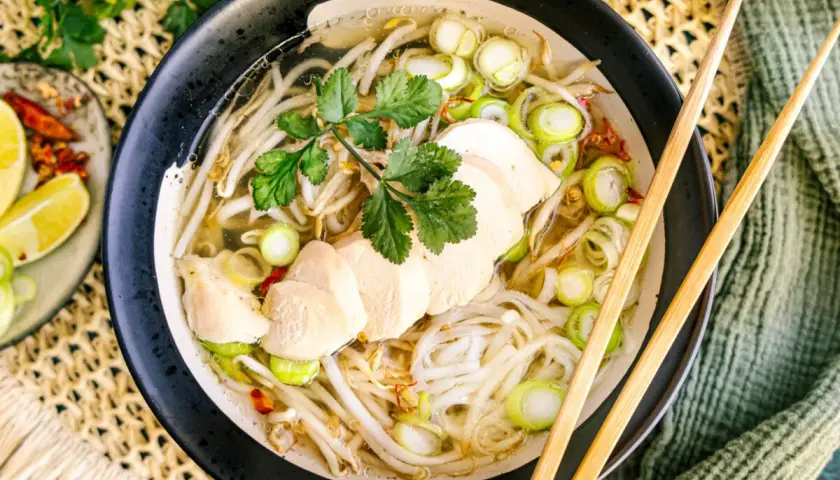 Eine dampfende Schüssel vietnamesische Reissuppe mit zarten Hühnerbrustscheiben, Reisnudeln, Sojasprossen und Frühlingszwiebeln.