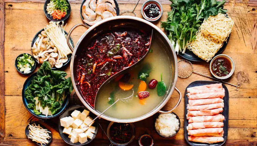 Eine köstliche asiatische Suppe mit zwei Brühen, Fleischscheiben, Garnelen, Pilzen, Gemüse, Tofu und Nudeln.