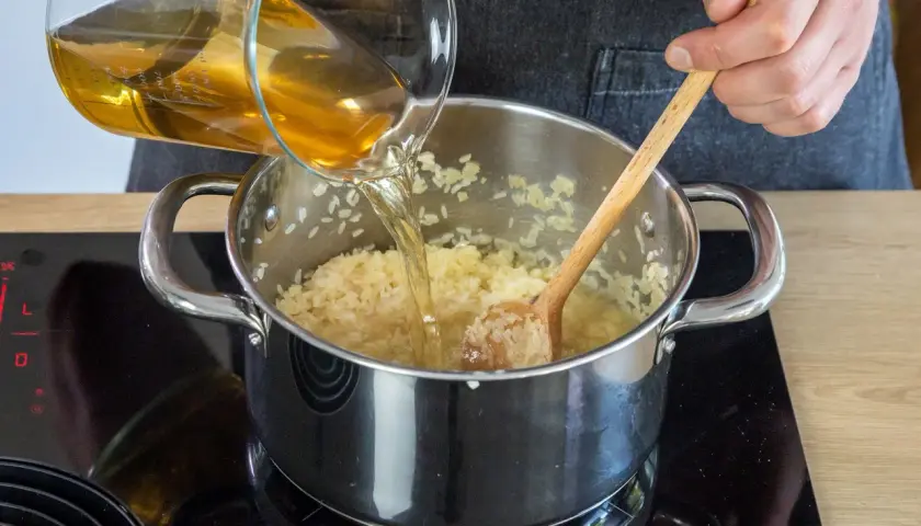 Flüssigkeit wird in einen Topf mit pilaw reis gegossen, während mit einem Holzlöffel gerührt wird.