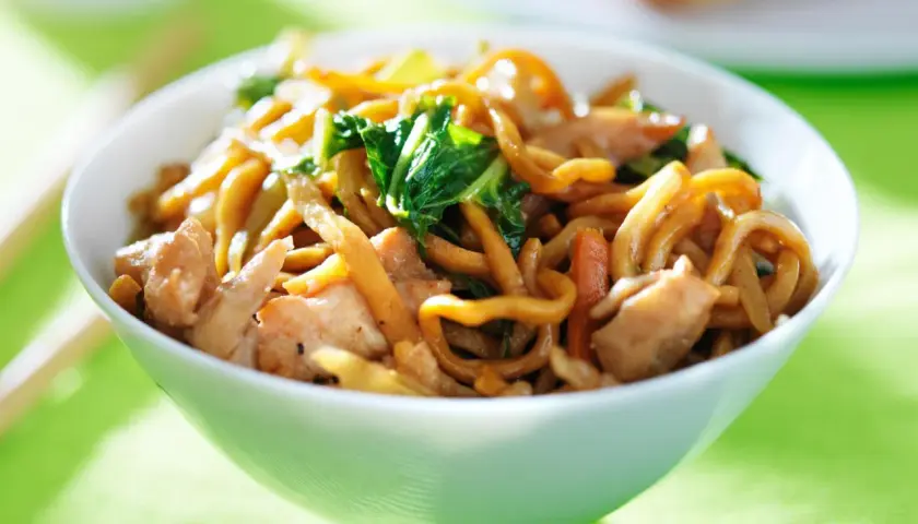 Eine Schüssel mit dampfenden Lo Mein Nudeln, Hühnchen und Gemüse, bereit zum Genießen.
