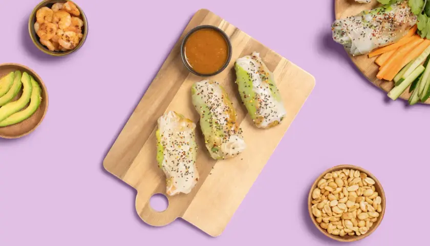 Frische Sommerrollen mit Hoisin-Sauce, Garnelen, Avocado und Erdnüssen auf lila Hintergrund.