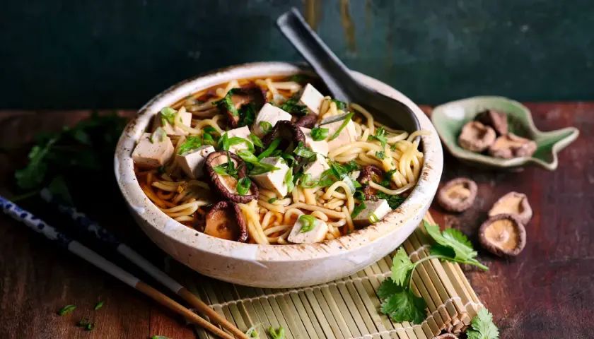 Herzhaftes Shiitake Ramen mit Tofuwürfeln und Frühlingszwiebeln in einer tiefen Schüssel, garniert mit Koriander.