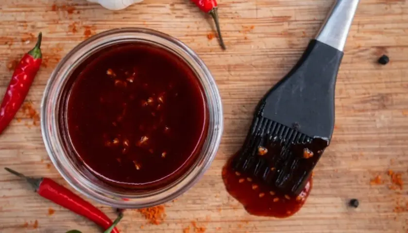 Hoisin-Sauce verwendung: eine Schüssel mit dunkler Sauce, dane ein Pinsel, dane rote Chilis und Knoblauch. Perfekt für Marinaden und Glasuren.