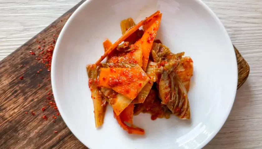 Frisch zubereitetes Kimchi, ein köstliches Rezept, serviert auf einem weißen Teller mit karamellisierten Karottenstreifen und Chinakohl.