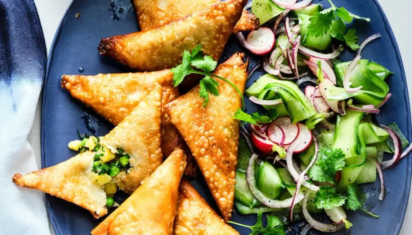 Goldbraune, knusprige Samosas mit Erbsen- und Kartoffelfüllung, serviert mit einem frischen Gurken-Radieschen-Salat. Ein leckeres samosas rezept.