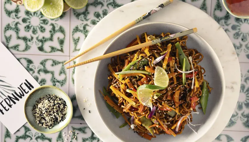 Asia Nudel mit Gemüse und Sesam, garniert mit Limettenspalten. Ein Gericht, das Fernweh weckt.