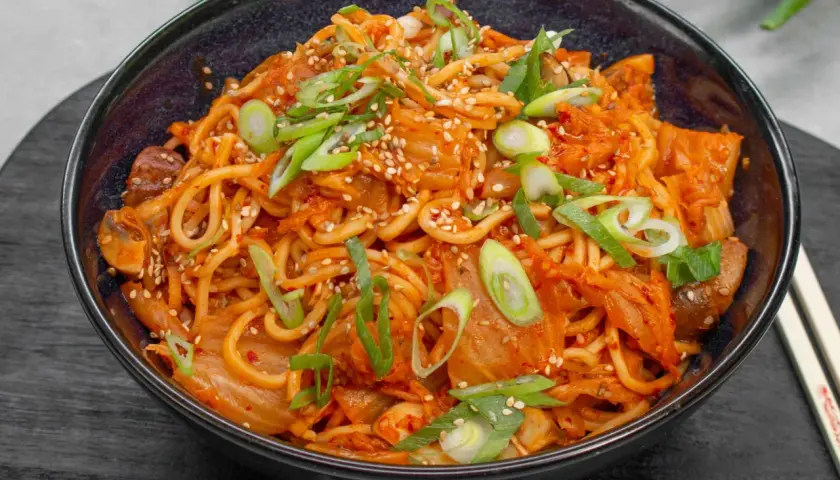 Eine Schüssel mit würzigem Kimchi Ramen, garniert mit Frühlingszwiebeln und Sesam.