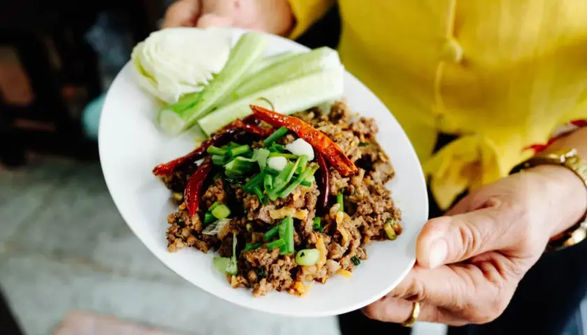 Würziges Laab Moo, ein thailändischer Hackfleischsalat, garniert mit Chili und Frühlingszwiebeln, serviert mit Gurken und Kohl.