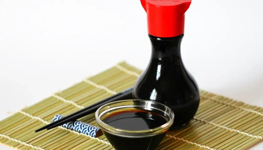 Eine Flasche chinesische Sauce mit Sojasauce, ein Schälchen und Stäbchen auf einer Bambusmatte.