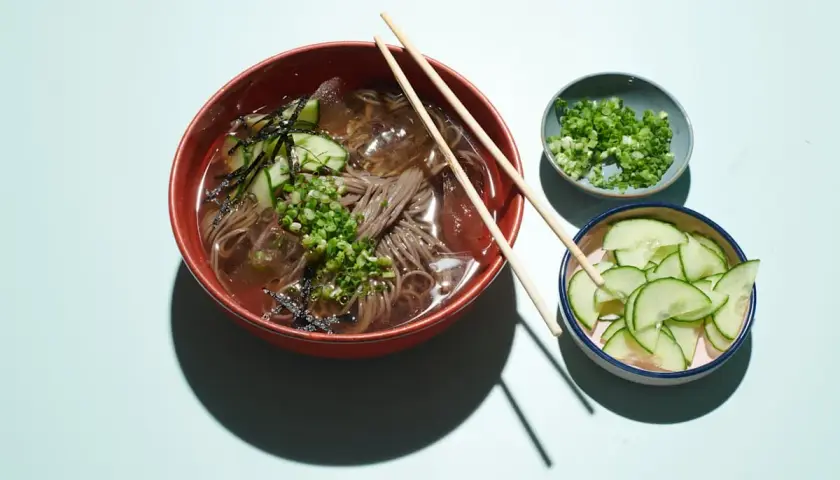Erfrischendes Mul Naengmyeon mit Buchweizennudeln, Gurkenscheiben, Frühlingszwiebeln und Seetang.
