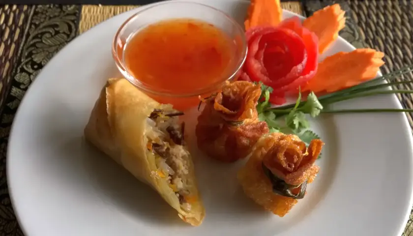 Knusprige Frühlingsrollen und Teigtaschen mit süß-saurer Sauce, garniert mit Karottenblumen. Ein köstlicher Nam Prik Genuss.