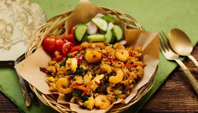 Ein authentisches nasi goreng rezept original mit Garnelen, Ei und frischem Gemüse. Serviert im Korbe, mit Gurken und Tomaten.