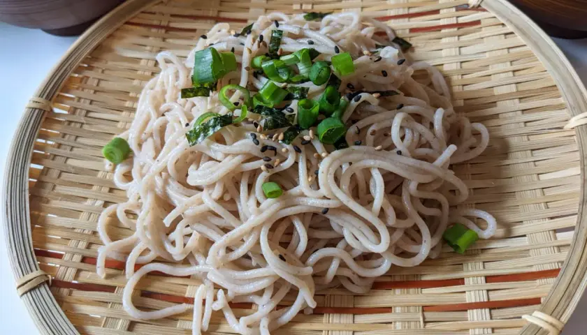 Ein köstlicher soba nudelsalat, garniert mit Frühlingszwiebeln und Sesam, serviert auf einem Bambusteller.