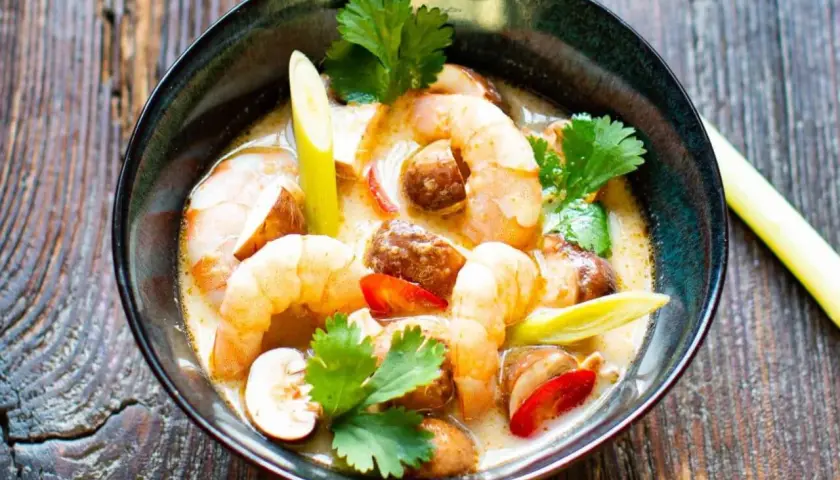 Eine Schüssel mit cremigem Tom Yam Gung, garniert mit Garnelen, Pilzen und Koriander.