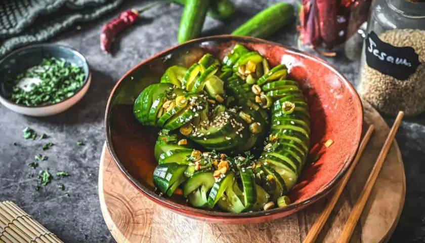 Schmackhafter Gurkensalat asiatisch, garniert mit Sesam und Kräutern, serviert in einer roten Schale mit Stäbchen.