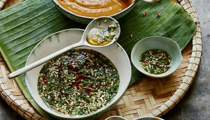 Schalen mit Saucen, darunter eine dunkle, würzige Sauce, die an Hoisin Sauce erinnert, und eine helle Erdnusssauce, auf Bananenblatt auf einem Korbtablett.
