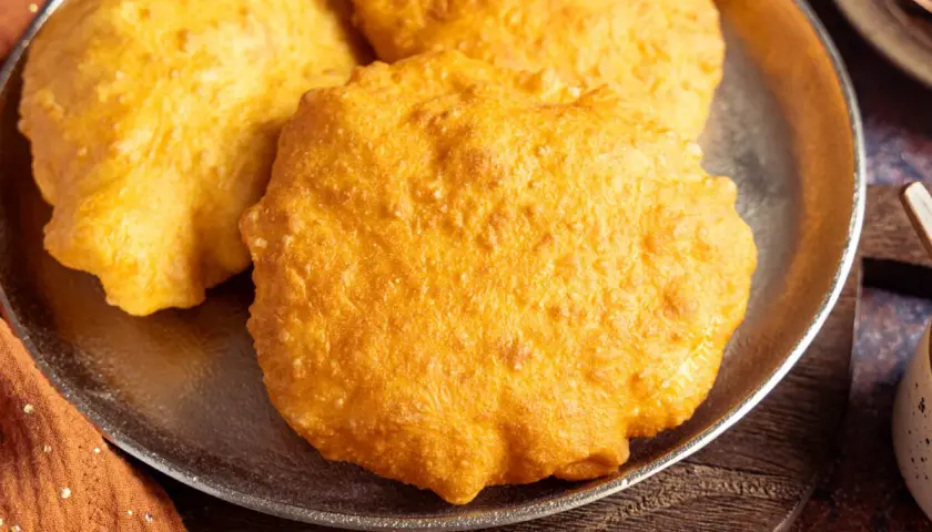 Drei goldbraune, fluffige Bhatura Brote liegen auf einem Teller. Sie sind frisch frittiert und duften herrlich.