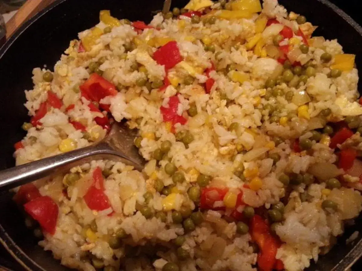 Ein köstlicher kantonesischer Reis mit Erbsen, Paprika und Mais, serviert in einer Pfanne.