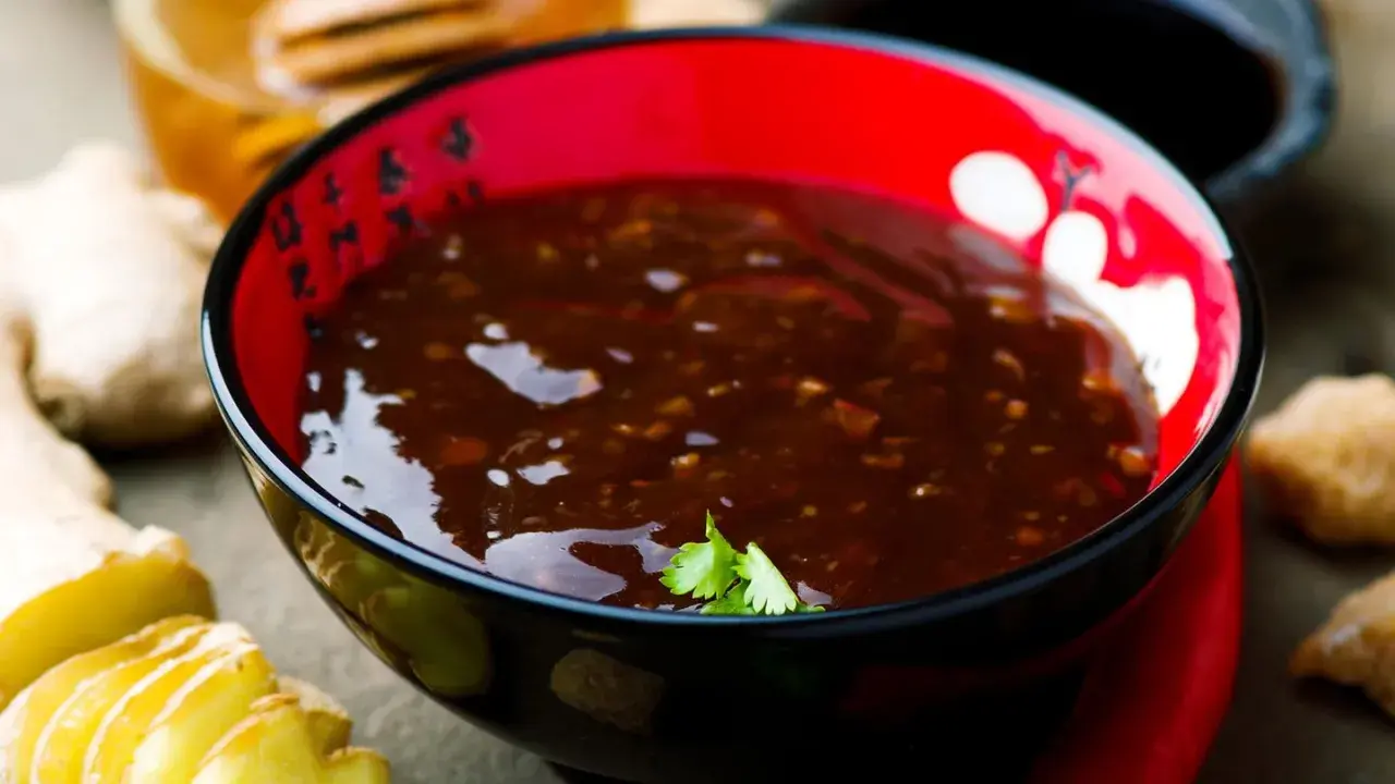 Schwarze Schale mit Teriyaki-Sauce, Ingwer und Honig. Der Geschmack von Teriyaki-Sauce ist süßlich-salzig und würzig.