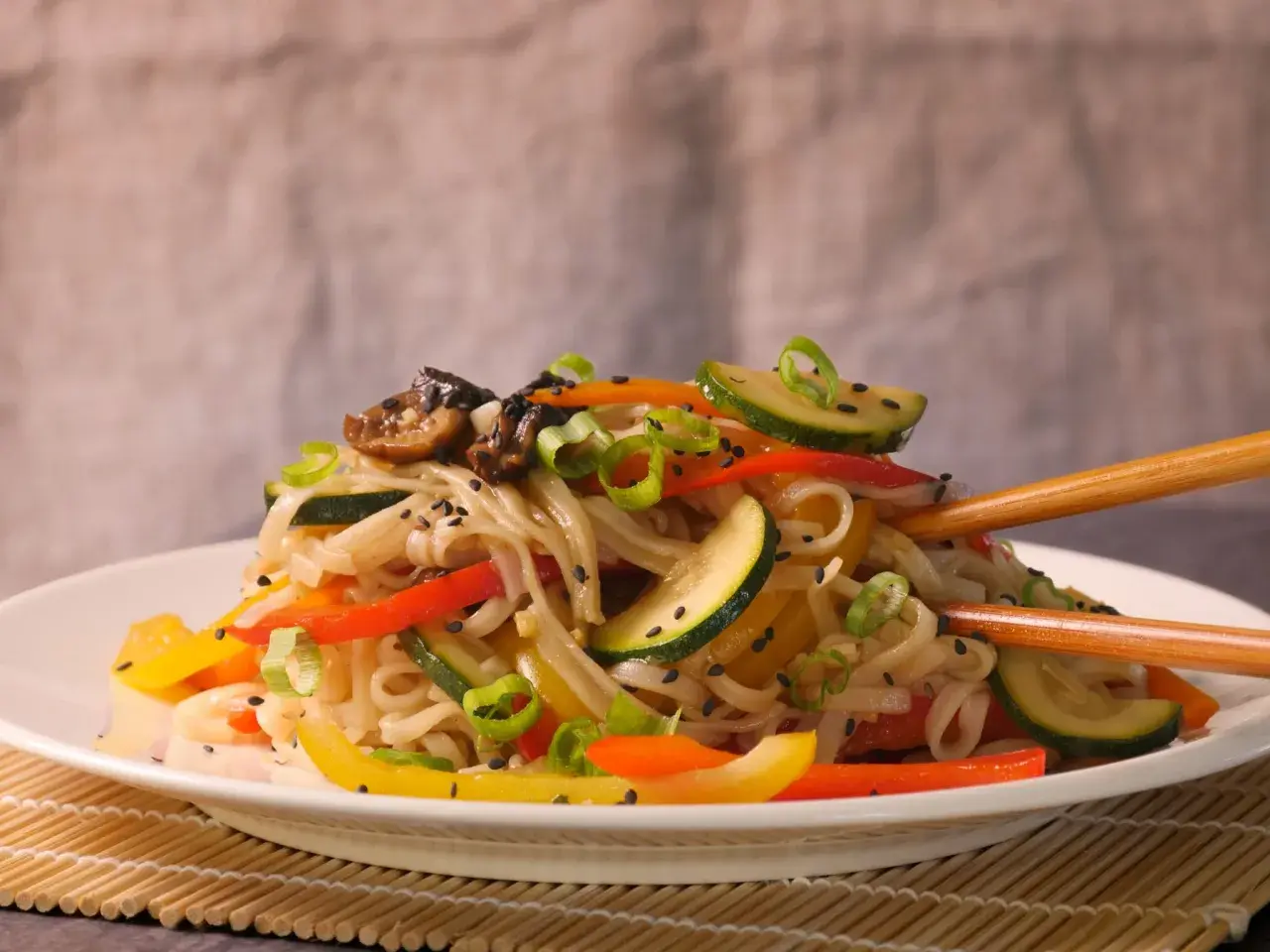 Reisnudeln mit bunten Paprikastreifen, Zucchini und Pilzen, garniert mit Frühlingszwiebeln und Sesam. Ein leckeres Gericht, das zum Genießen einlädt.