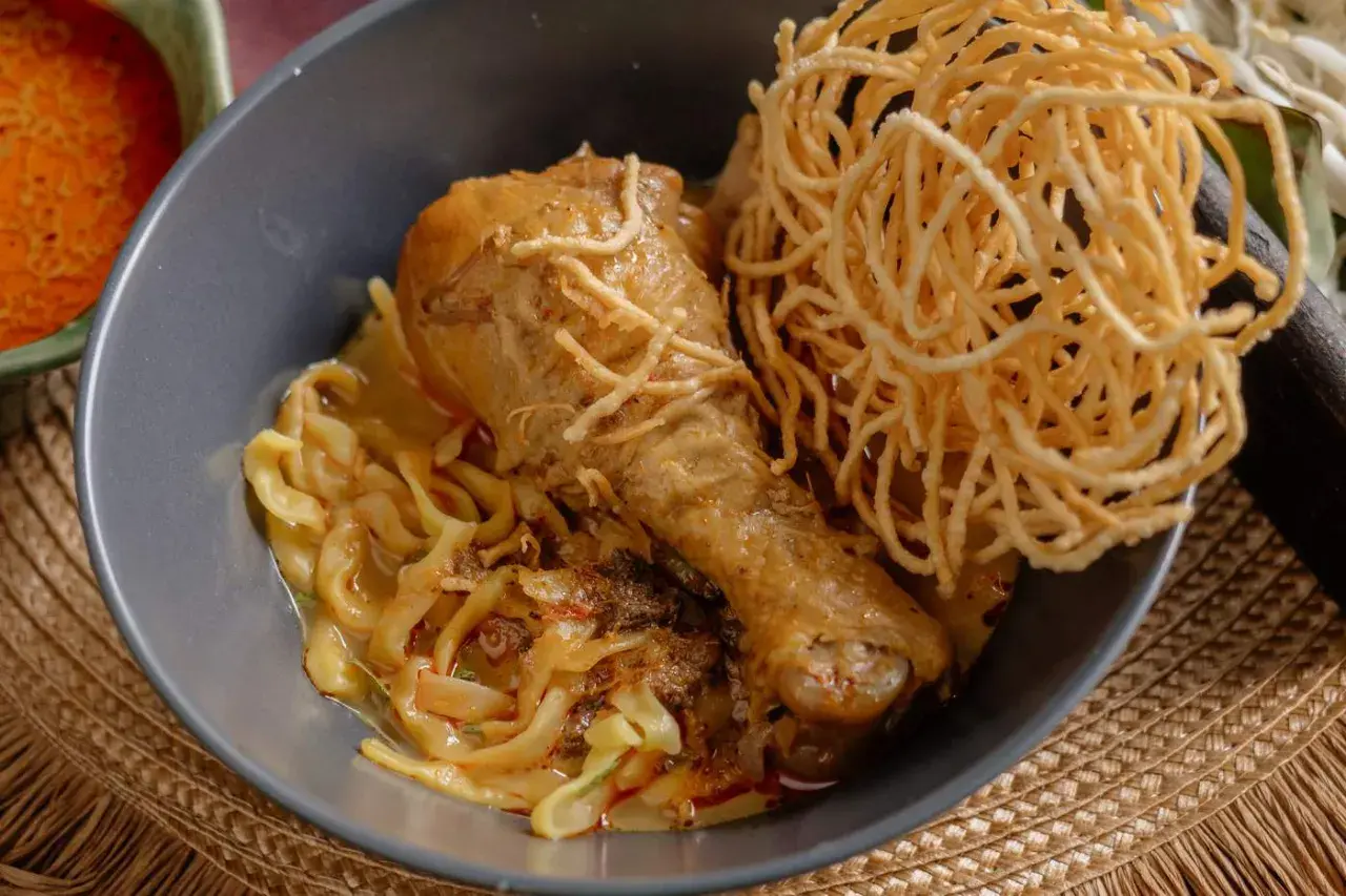 Khao Soi: ein Hühnerbein auf Nudeln in cremiger Kokosmilch-Currysauce, garniert mit knusprigen Nudeln.