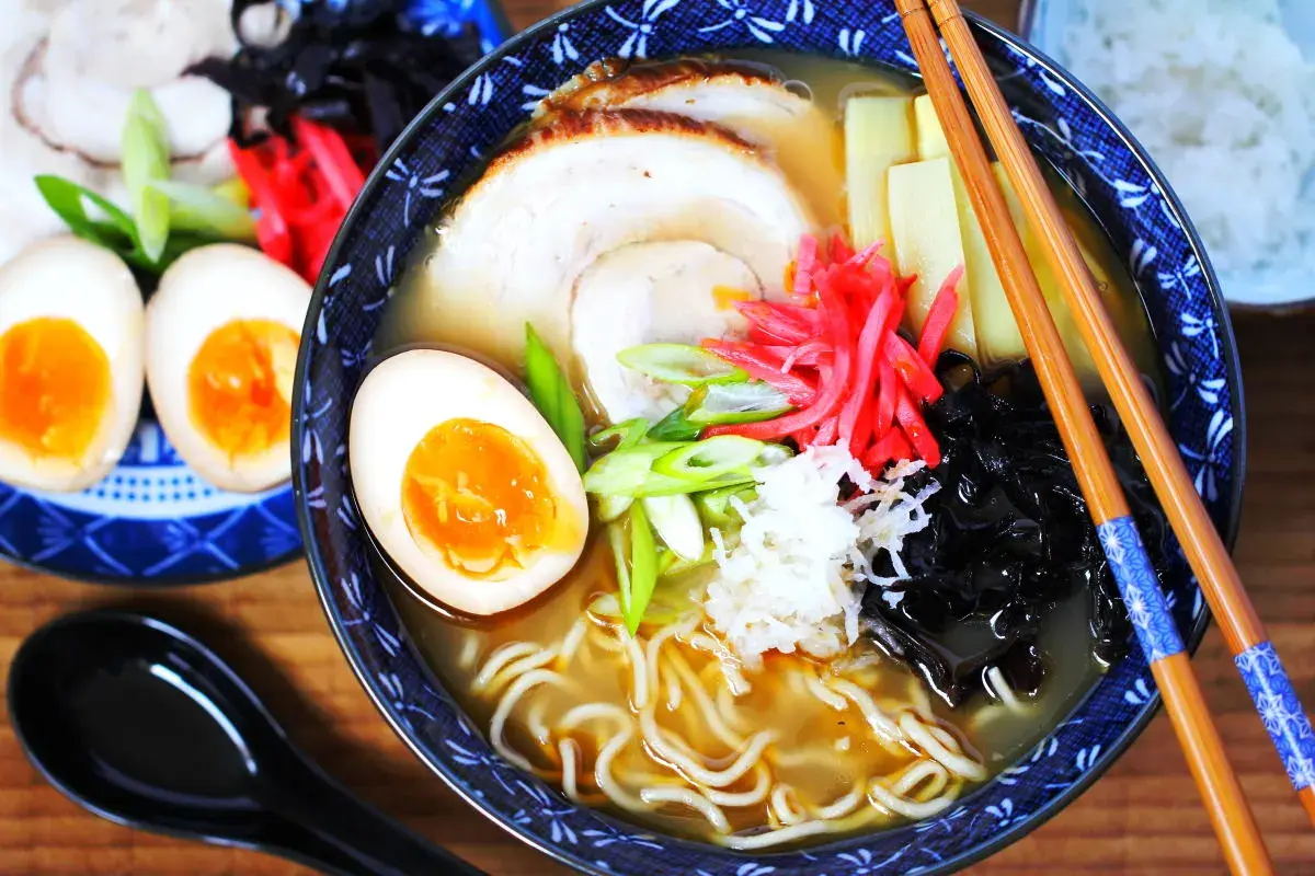Eine Schüssel Ramen mit perfekt gekochten ramen eiern, Schweinefleisch, Bambussprossen und Frühlingszwiebeln. Daneben liegen weitere halbe Eier.